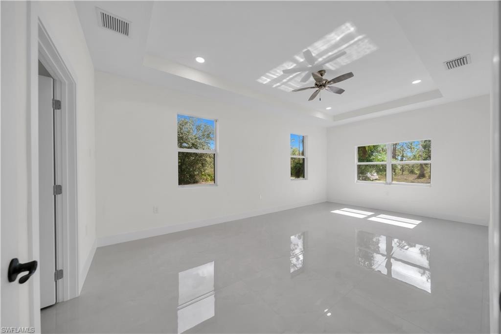 Master bedroom with light-toned tile flooring, a tray ceiling with recessed lighting, and a ceiling fan