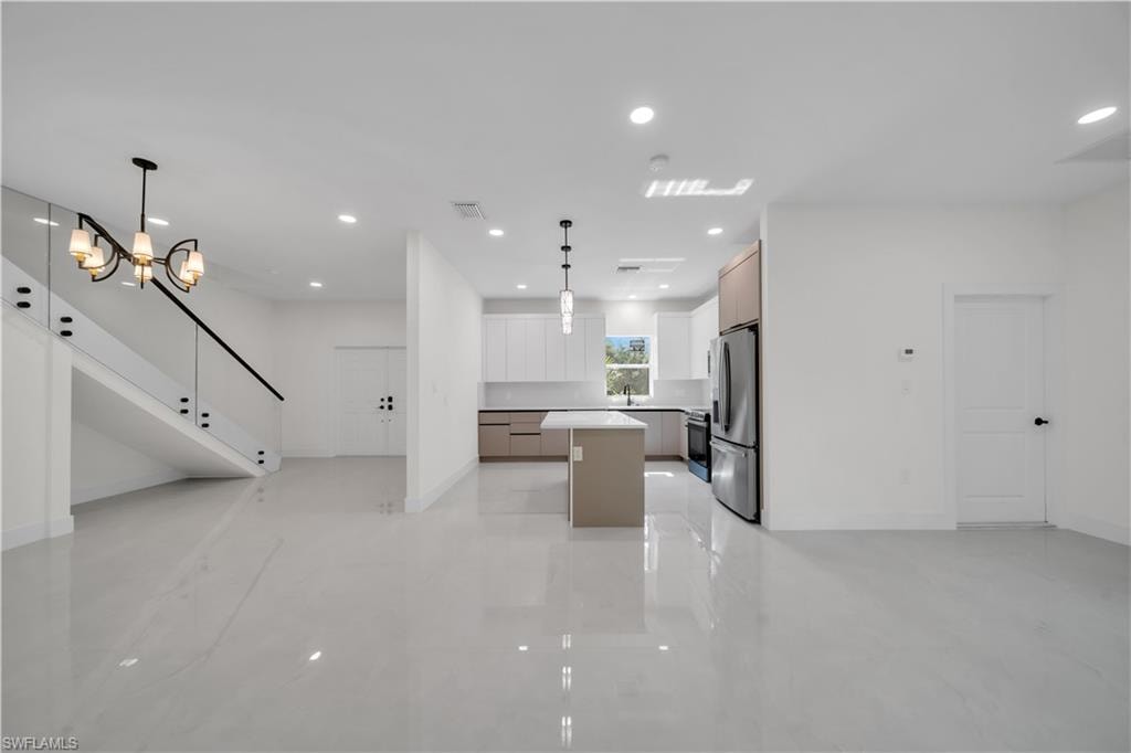 Open-concept living area featuring white tile flooring, a modern chandelier, and a glass-paneled staircase with a black handrail