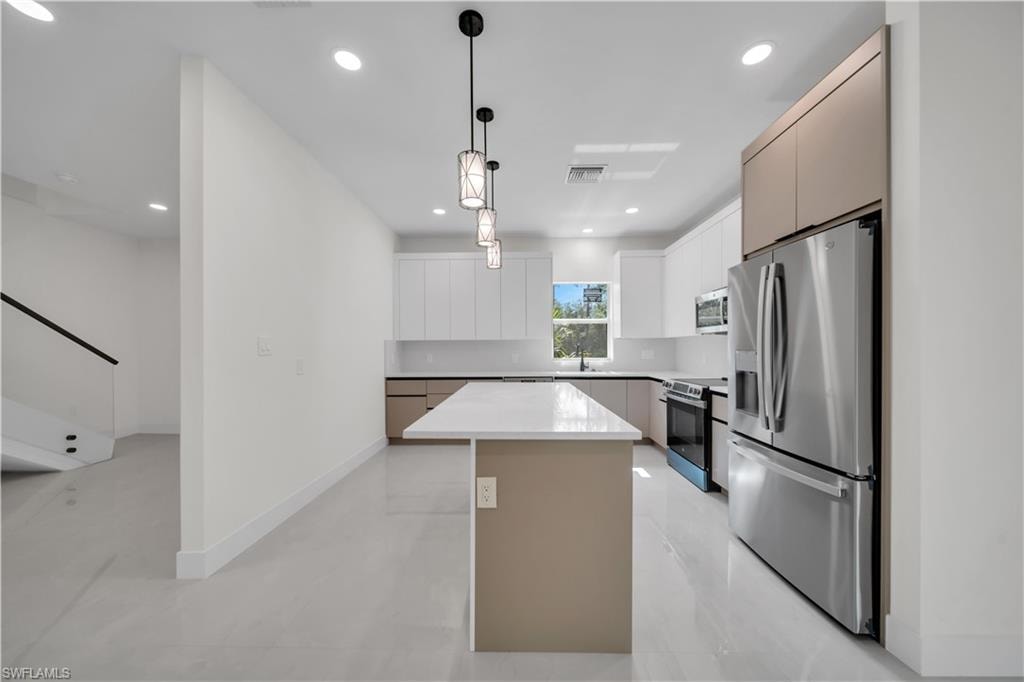 Modern kitchen featuring a central island with a light-toned countertop, white cabinetry, integrated stainless steel appliances, contemporary pendant lighting, and light-colored tile flooring