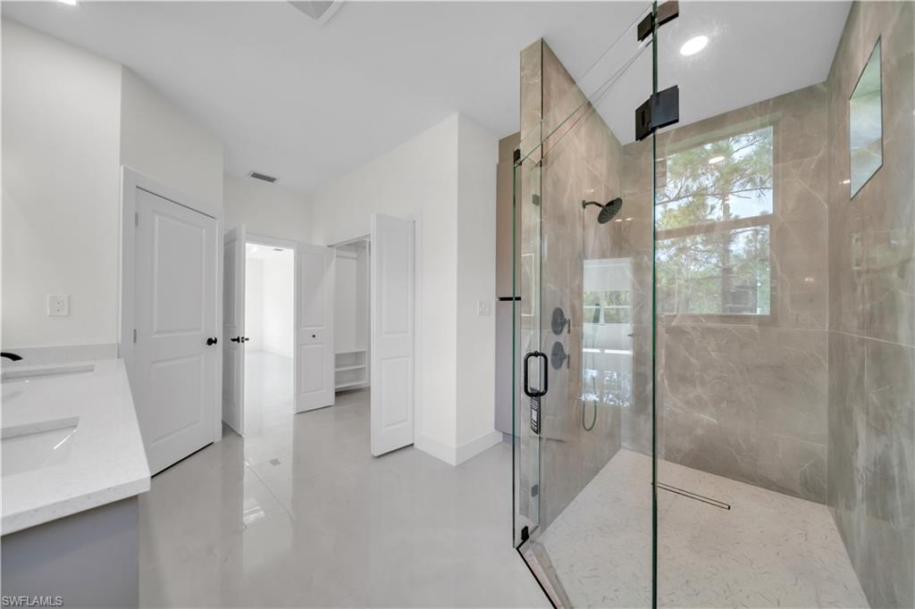 Spacious master shower  featuring a glass-enclosed area with tiled walls , dual vanity with undermount sinks and quartz countertops, and light-toned floor tiling