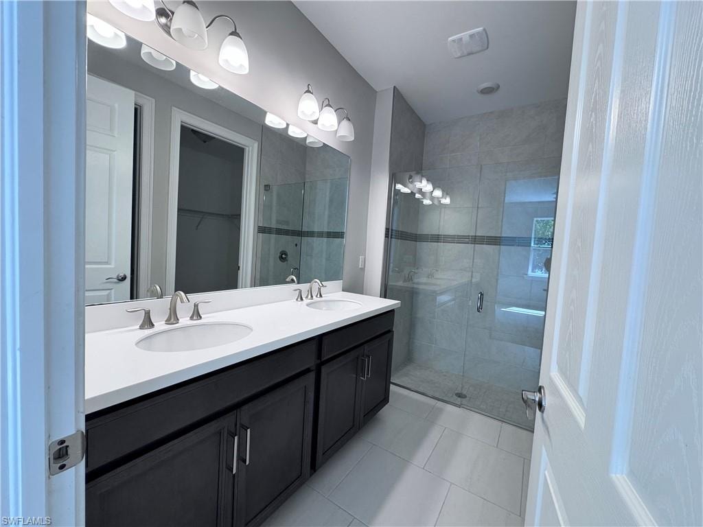 Bathroom featuring a shower stall, light tile patterned floors, double vanity, and a spacious closet