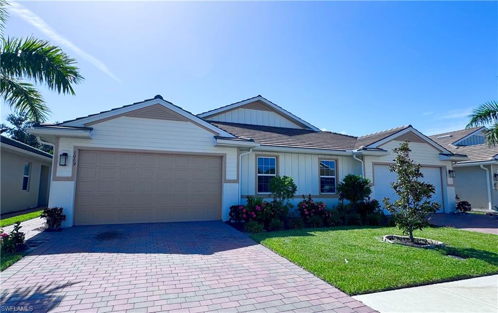 Ranch-style home with a garage, decorative driveway, board and batten siding, and a front yard