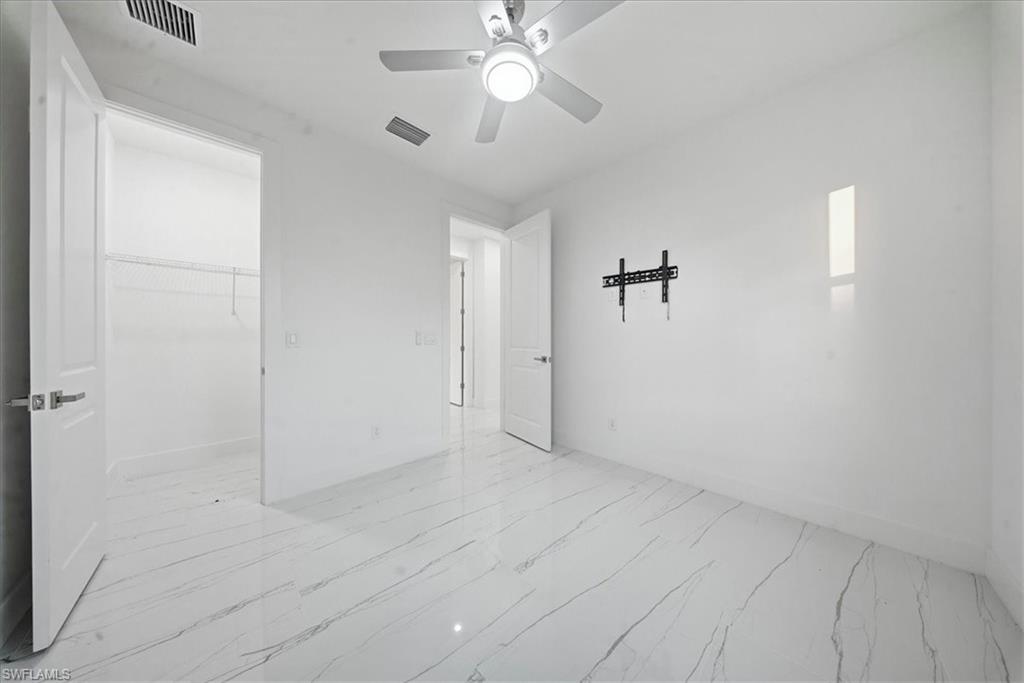 Light-filled room featuring large format tile flooring, a ceiling fan with integrated lighting, a wall-mounted television bracket, and an adjacent walk-in closet with wire shelving