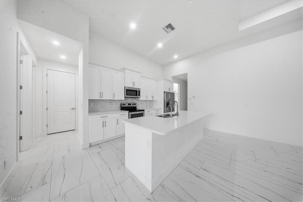 Modern kitchen featuring white cabinetry, stainless steel appliances, a white tile backsplash, and a central island with an undermount sink