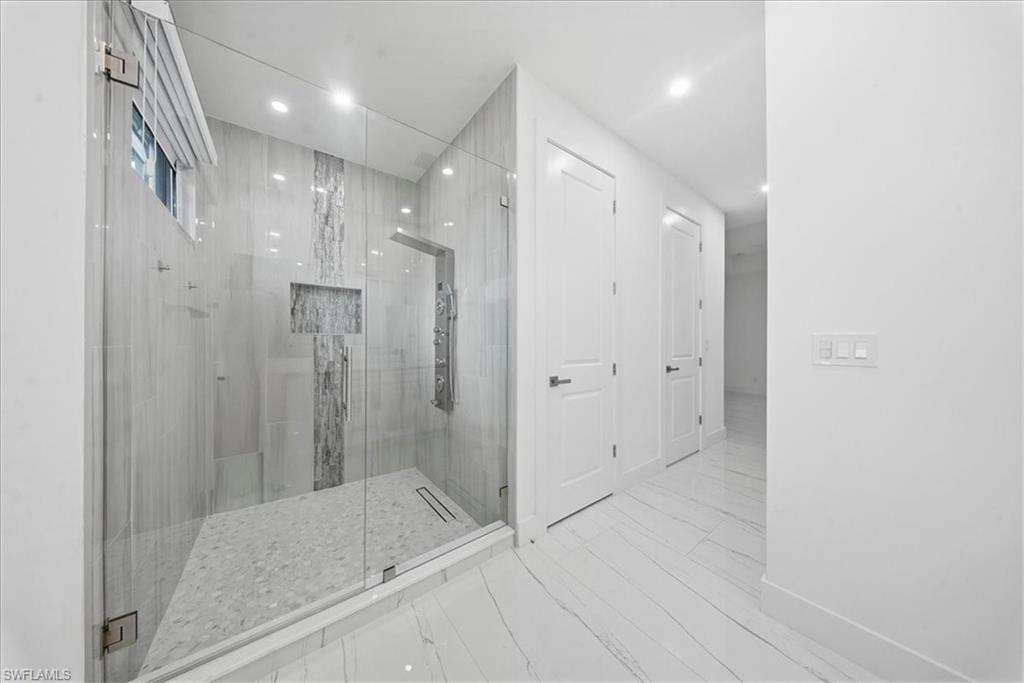 Spacious shower enclosure with glass surround, featuring large format tile walls, a vertical accent tile stripe, and a recessed niche