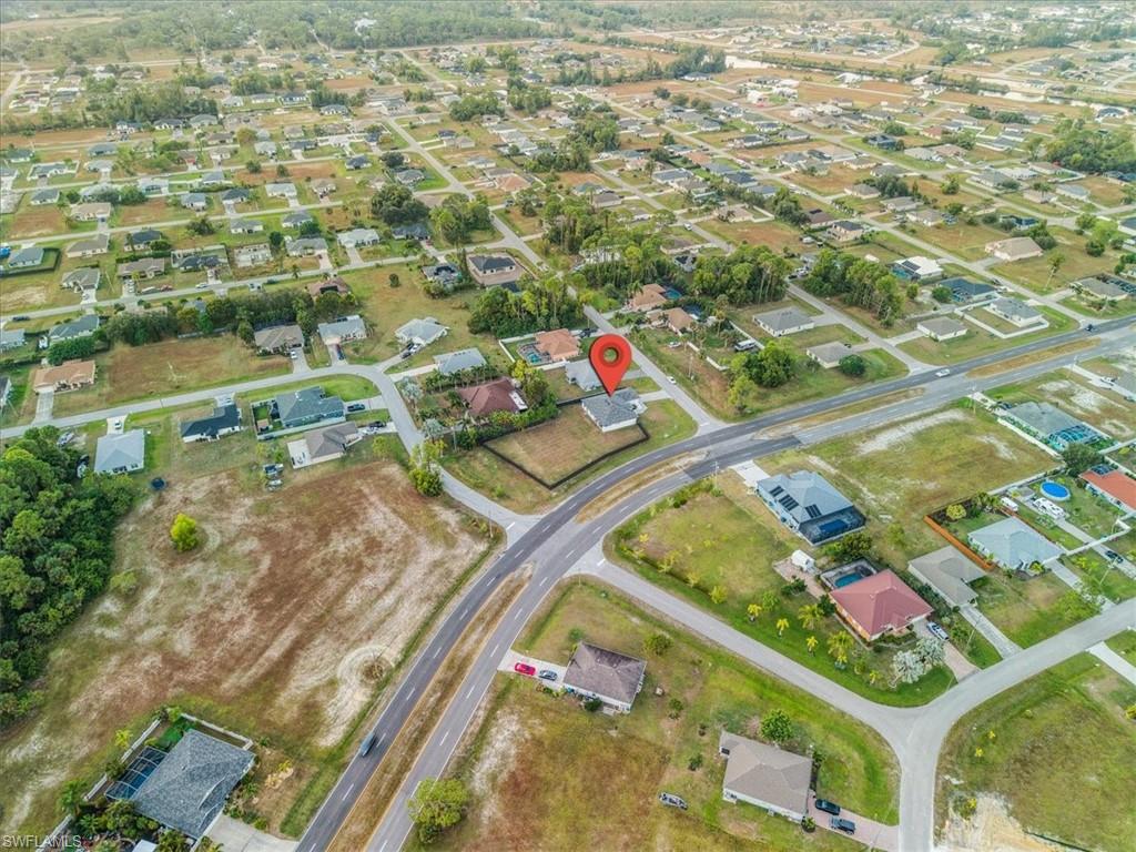 Aerial view of a residential neighborhood with single-story homes, paved roads, and undeveloped land parcels