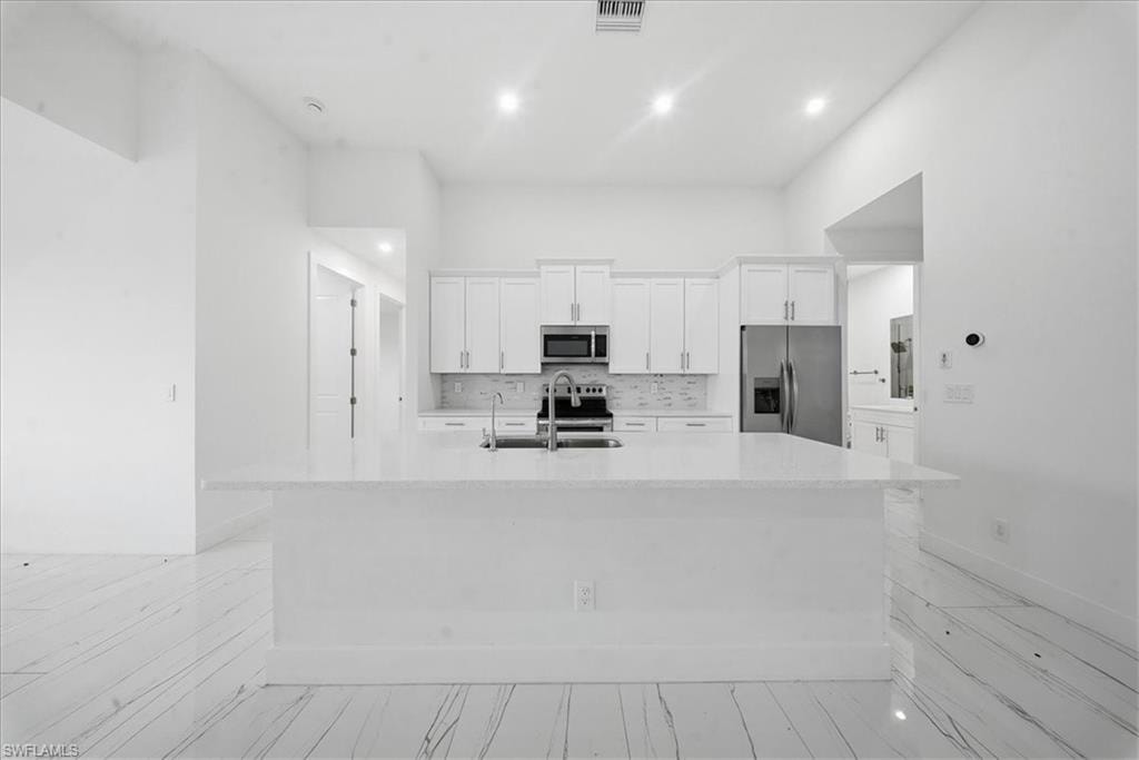 Modern kitchen featuring a large center island with a quartz countertop, white shaker cabinetry, stainless steel appliances, and a tiled backsplash