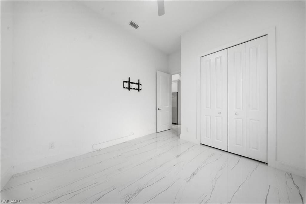 Room featuring light-toned walls, white bi-fold closet doors, a ceiling fan, and white flooring with dark veining