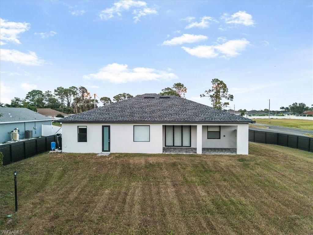 Rear exterior with white stucco finish, dark shingle roof, and a covered patio area