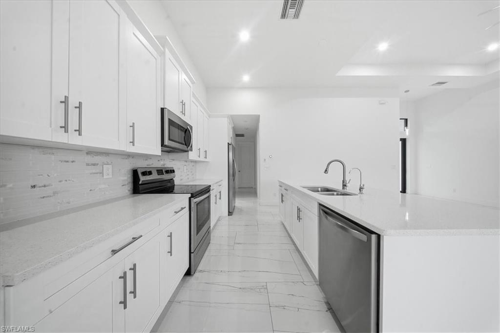 Contemporary kitchen featuring white shaker cabinetry, stainless steel appliances, light-toned countertops, a textured backsplash, and large format tile flooring