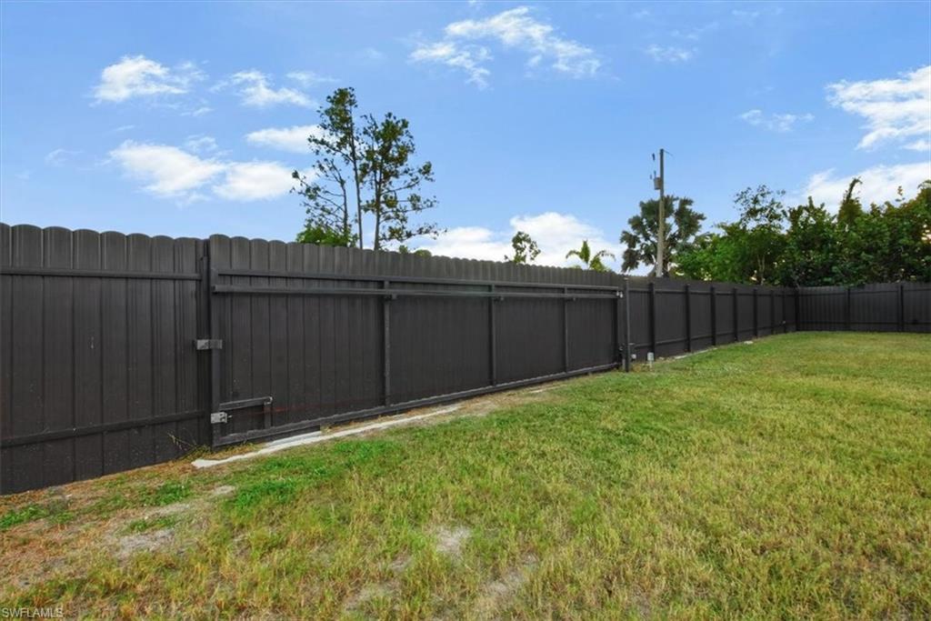 Expansive backyard featuring a dark privacy fence with a rolling gate, manicured lawn, and mature trees in the background