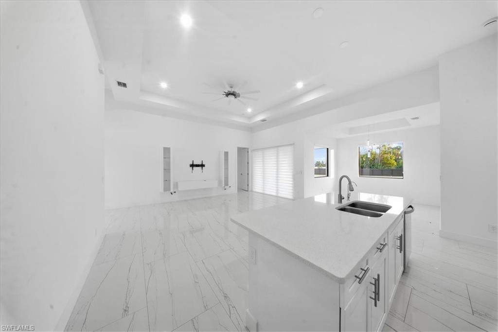 Spacious open-concept interior featuring a central island with an undermount dual sink and a pull-down faucet, white cabinetry with silver-tone hardware, and light-toned flooring