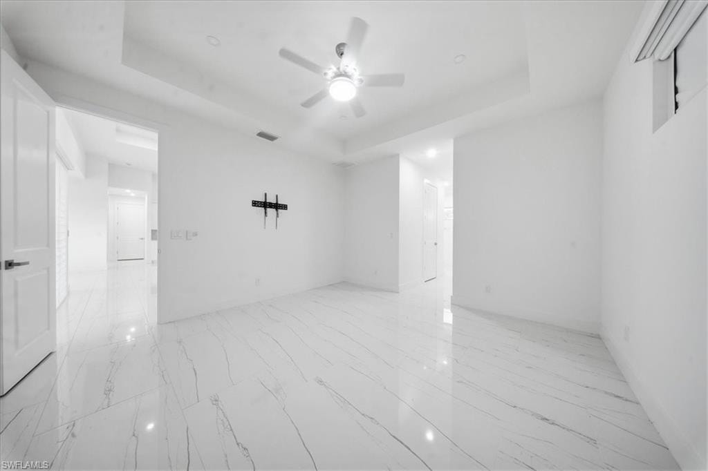 Spacious room featuring white tile flooring with gray veining, a tray ceiling, and a ceiling fan with integrated lighting