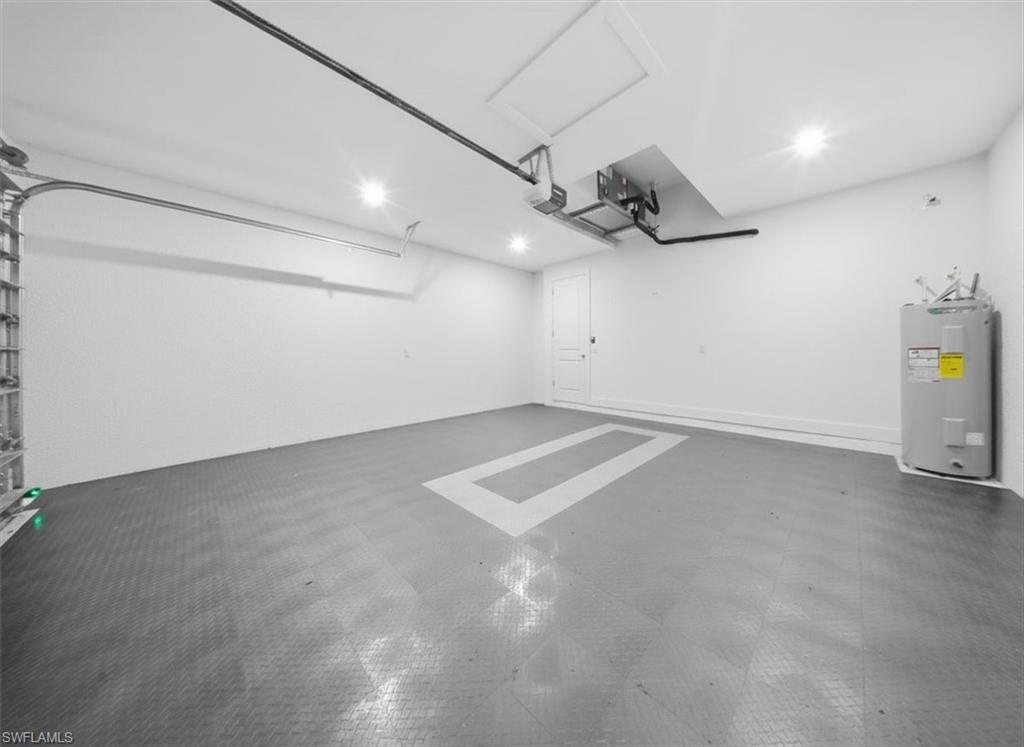 Spacious garage featuring durable interlocking floor tiles, a built-in water heater, and overhead lighting