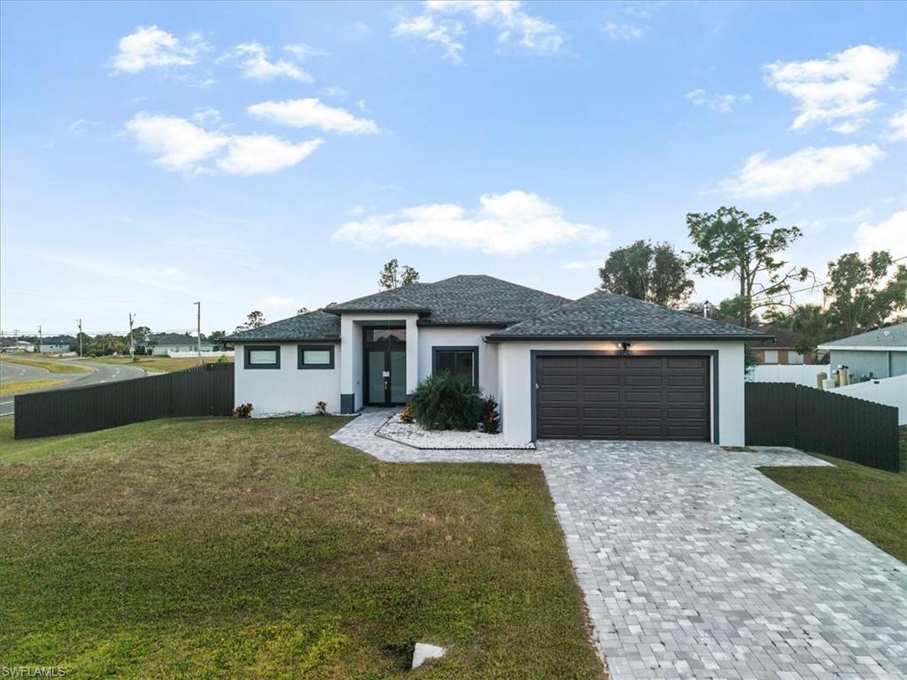 Modern stucco exterior featuring a dark brown garage door, a paved driveway, and a fenced yard