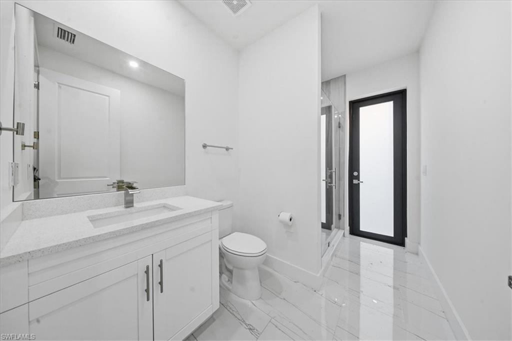 Modern bathroom with a white vanity and integrated sink, a large mirror, a glass-enclosed shower, a black framed interior door, and marble-look tile flooring