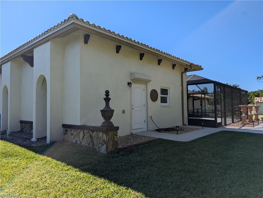 Back of property featuring a lawn, glass enclosure, and a patio area