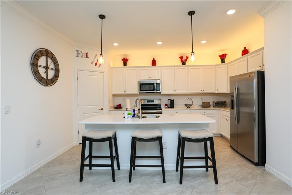 Kitchen with an island with sink, sink, white cabinetry, stainless steel appliances, and crown molding
