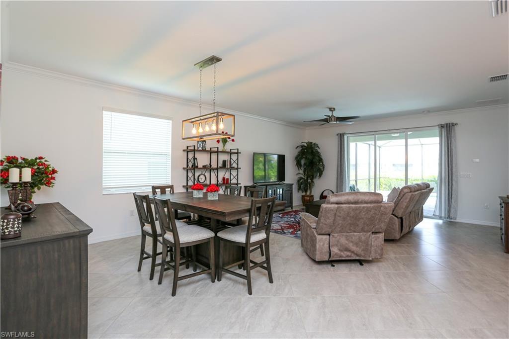 Tiled dining space with ceiling fan with notable chandelier and crown molding