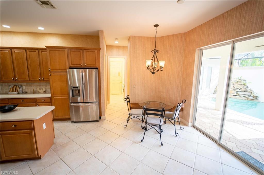 Kitchen with pendant lighting, a notable chandelier, stainless steel refrigerator with ice dispenser, backsplash, and light tile patterned floors