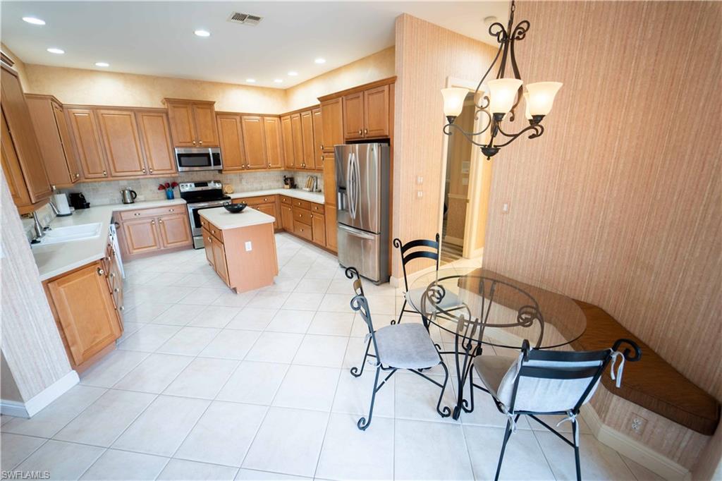 Kitchen with pendant lighting, a chandelier, tasteful backsplash, a kitchen island, and appliances with stainless steel finishes