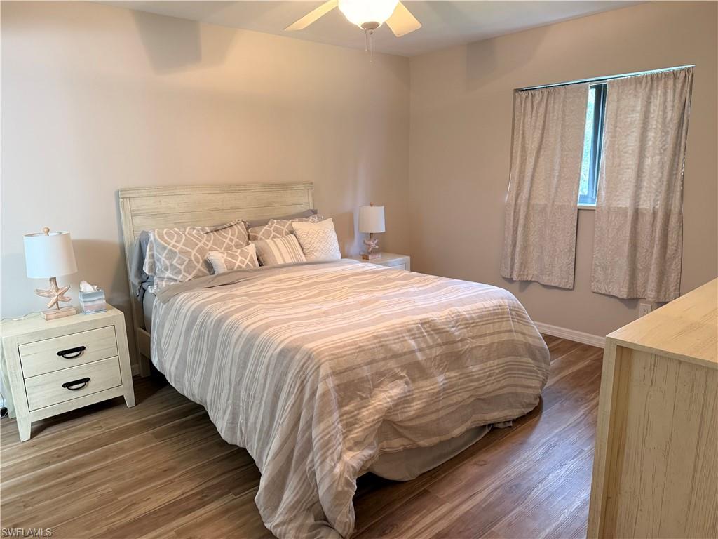 Neutral wall tones, wood-finish flooring, and a ceiling fan with light fixture enhance this bedroom space
