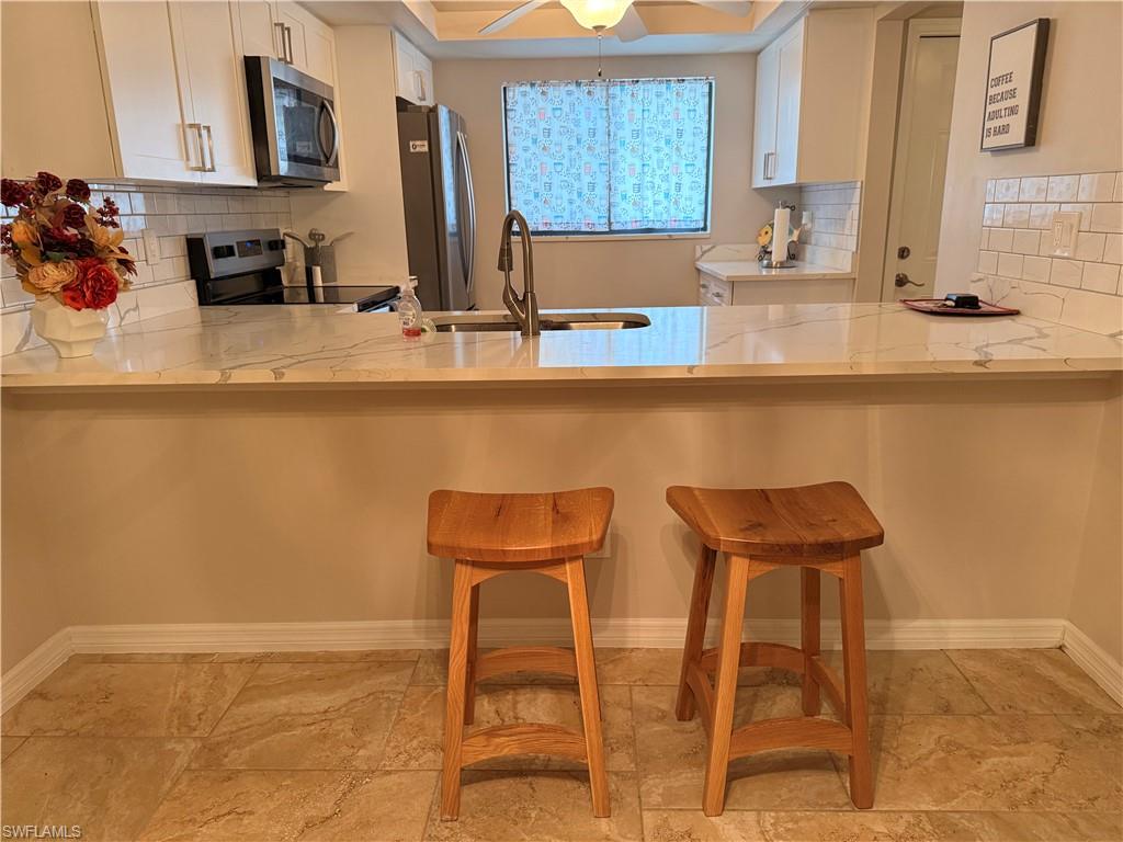 Kitchen featuring a breakfast bar with stone-finish countertops, white shaker-style cabinetry, and a subway tile backsplash