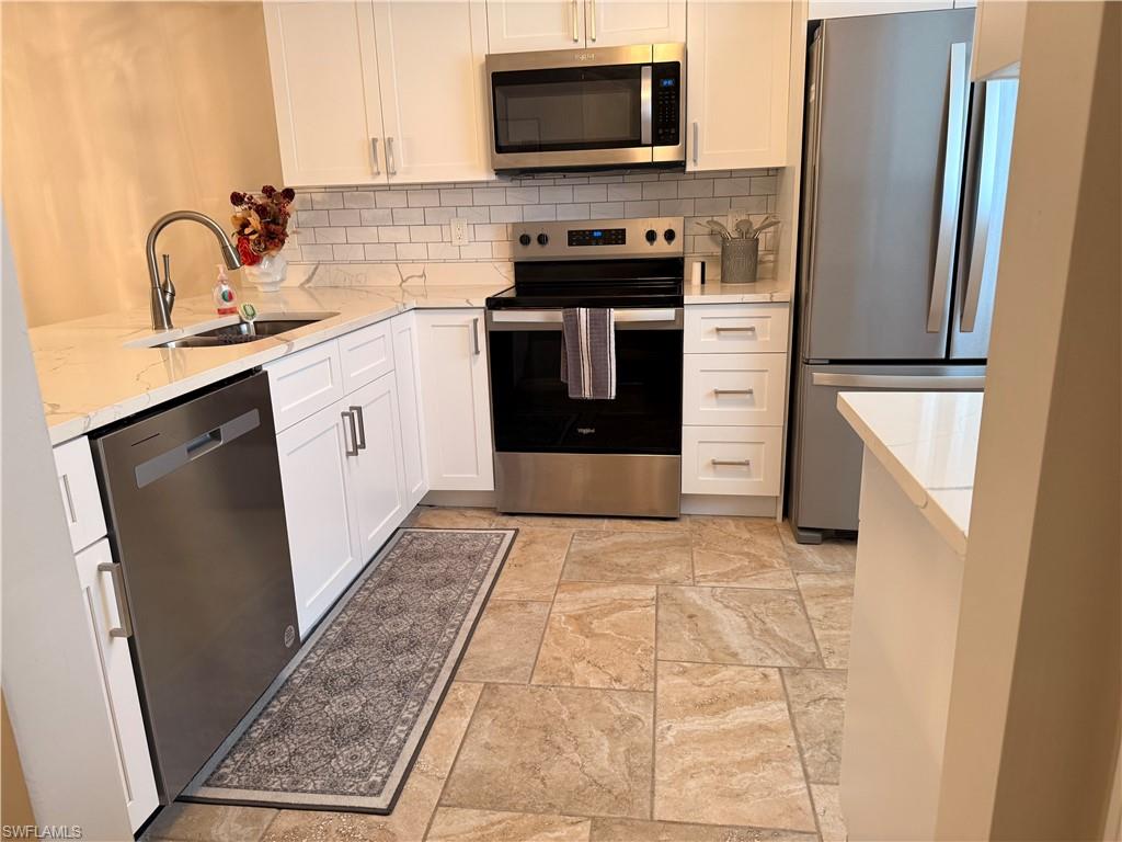Modern kitchen featuring white shaker cabinetry, stainless steel appliances, white subway tile backsplash, and light-toned stone-finish flooring