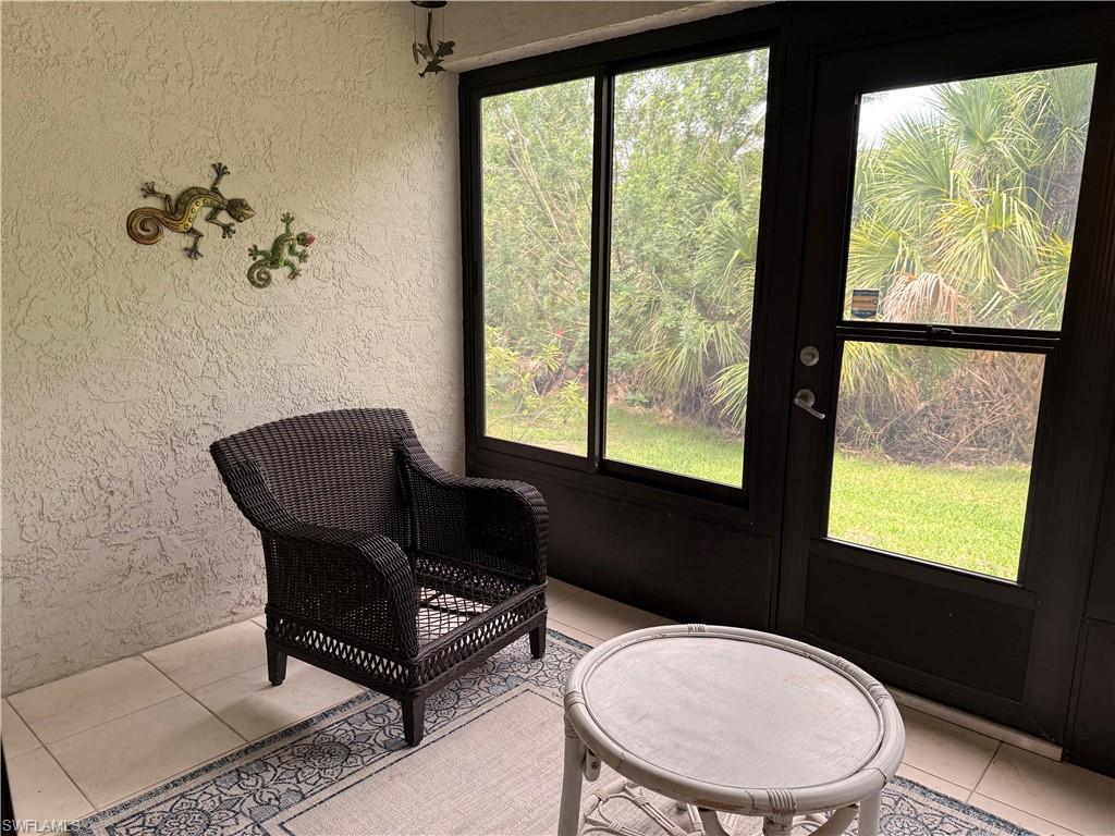 Screened patio featuring a textured stucco wall, tile flooring, and a dark-framed glass door with multiple lites