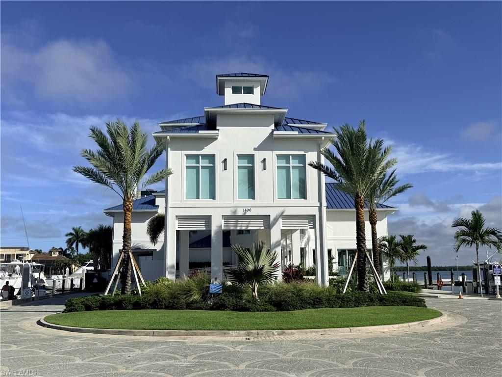White exterior with a blue metal roof, prominent cupola, and mature palm trees