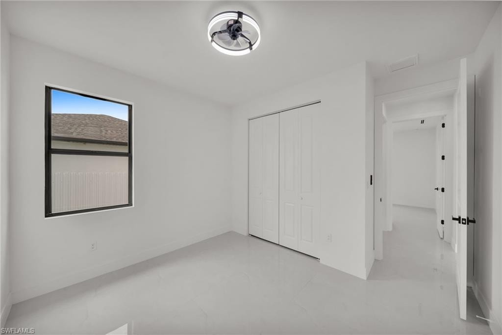 Room featuring light gray tile flooring, a window with black trim, a ceiling-mounted light fixture with fan, and bi-fold closet doors