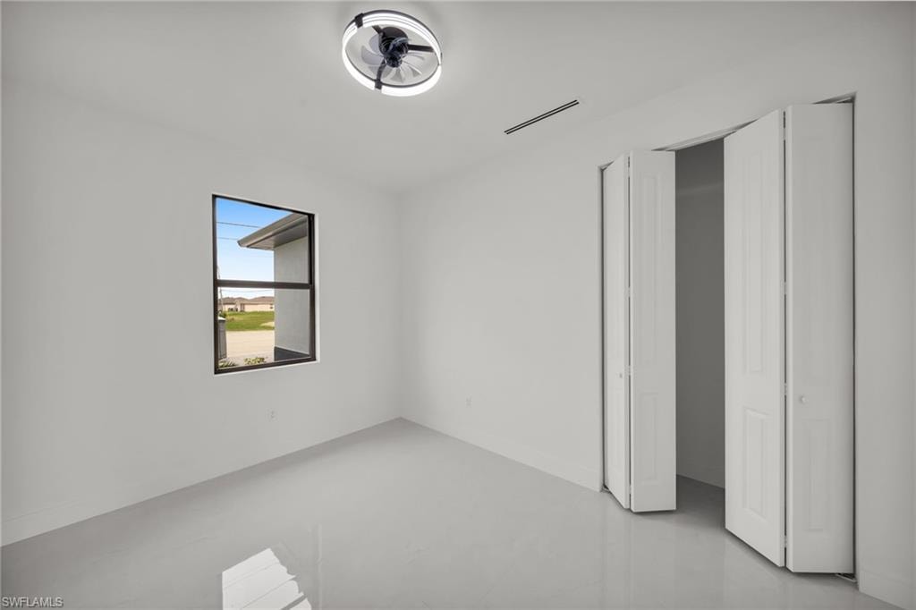 Bright interior space featuring a modern ceiling fan with integrated lighting, a dark-framed window, sleek light gray flooring, and white bi-fold closet doors