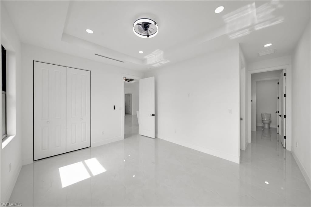 Spacious room featuring white tile flooring, bi-fold closet doors, a tray ceiling with recessed lighting, and a modern ceiling fan
