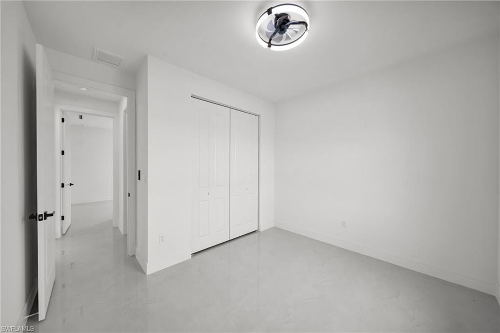 Spacious room featuring light-toned flooring, white walls, and a modern ceiling light fixture