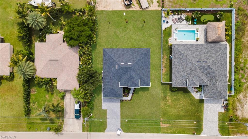 Aerial perspective showcasing the property's rectangular lot, an expansive green lawn, and a light-colored paved driveway