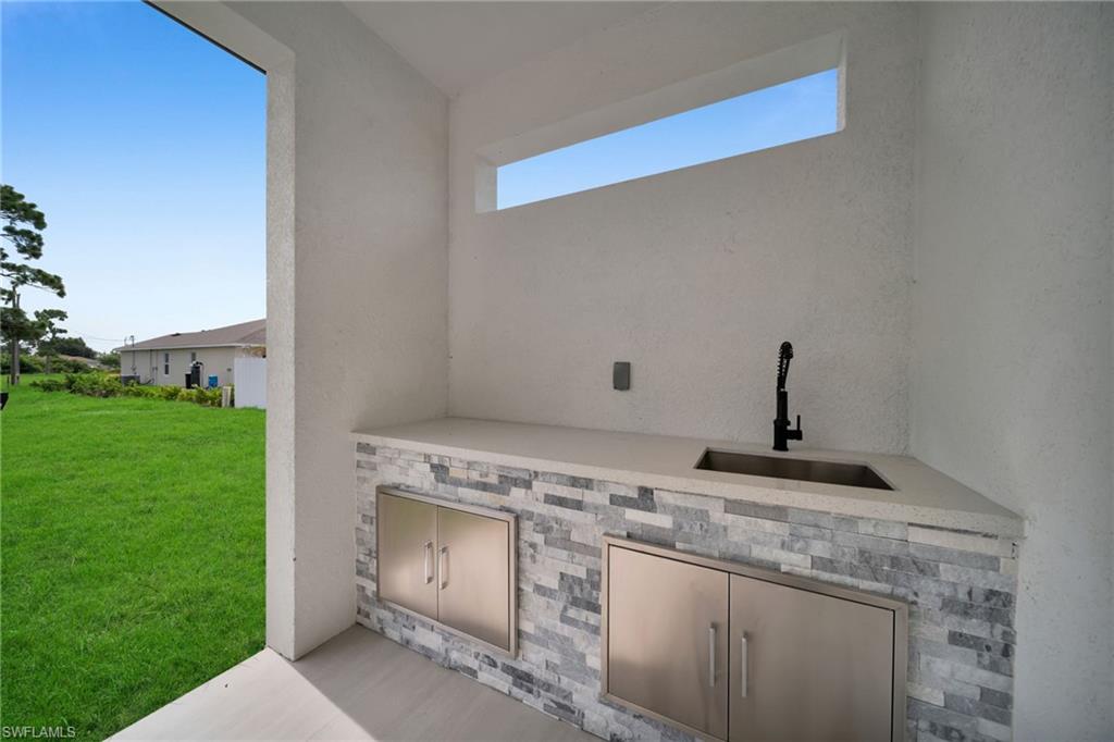 Outdoor kitchen featuring a stone accent wall, countertop with integrated sink, modern black faucet, and stainless steel cabinet doors