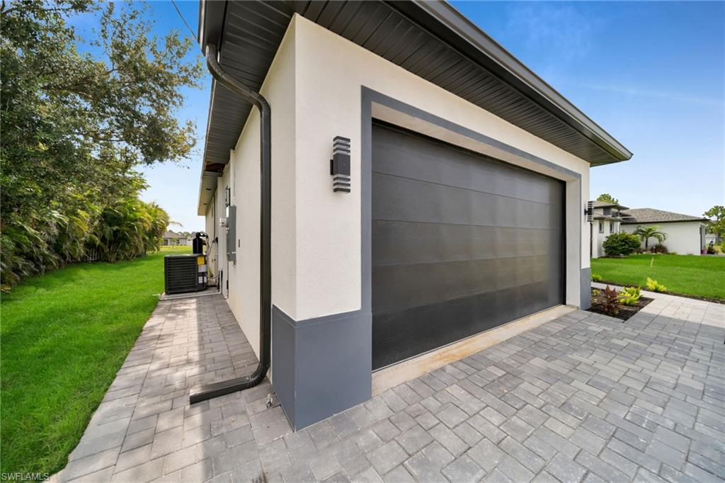 Exterior featuring a modern dark gray garage door framed by white stucco and dark gray trim, paver driveway, and contemporary exterior lighting fixtures