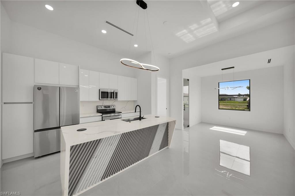 Modern kitchen featuring a waterfall island with a patterned base, stainless steel appliances, recessed lighting, and sleek white cabinetry