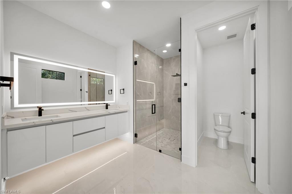 Spacious modern bathroom featuring a floating double vanity with under-cabinet lighting, illuminated mirror, and matte black fixtures