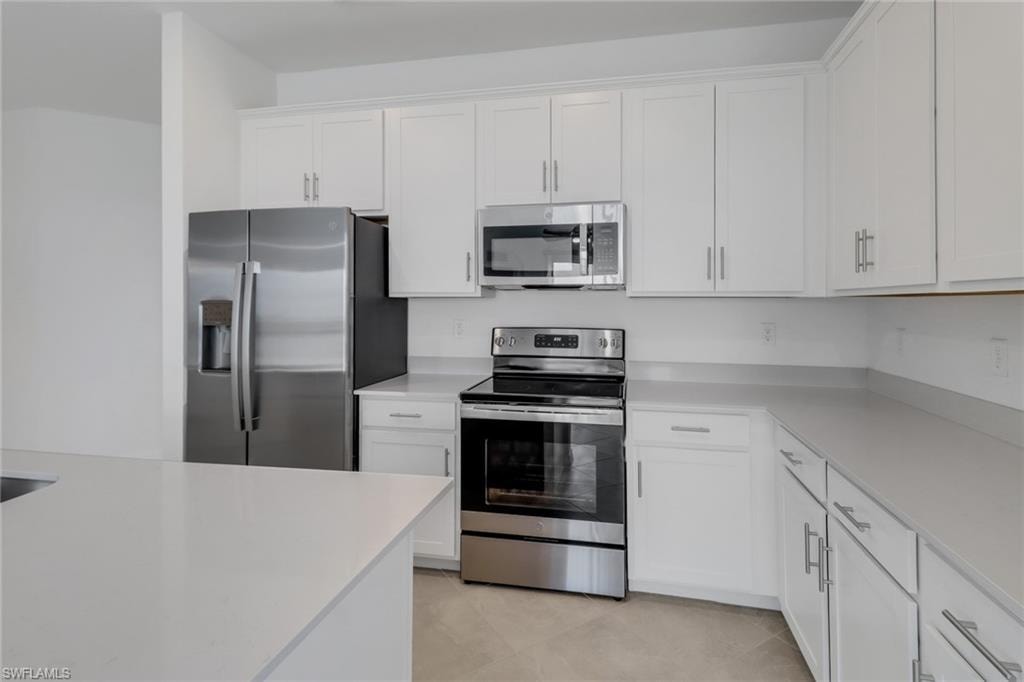 Modern kitchen featuring white shaker cabinetry, stainless steel appliances, light-toned countertops, and an integrated kitchen island