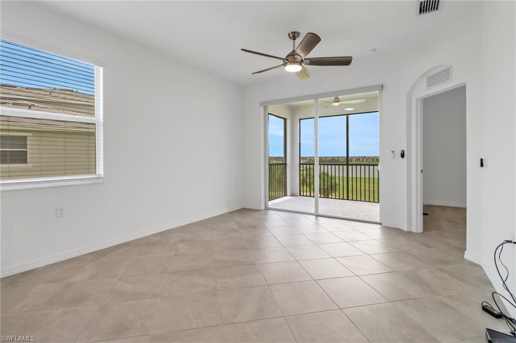 Spacious room featuring neutral tile flooring, a ceiling fan, and a large window with blinds