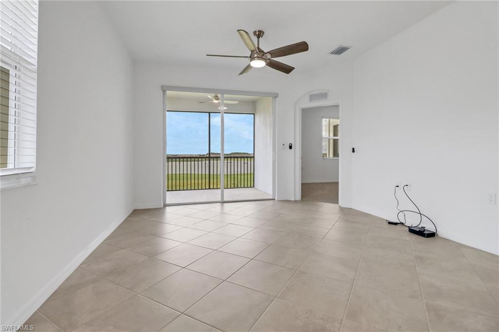Spacious room featuring neutral tile flooring, a ceiling fan with integrated lighting, and a large sliding glass door opening to a screened balcony overlooking a natural landscape