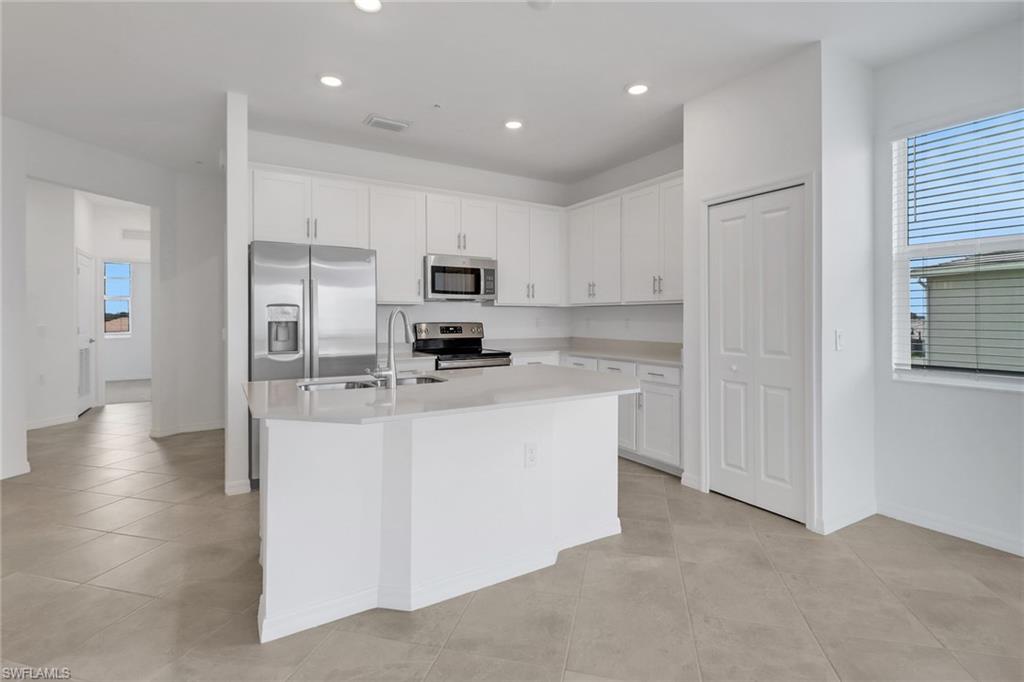 Modern kitchen featuring white cabinetry, a central island with a sink, stainless steel appliances, recessed lighting, and tile flooring
