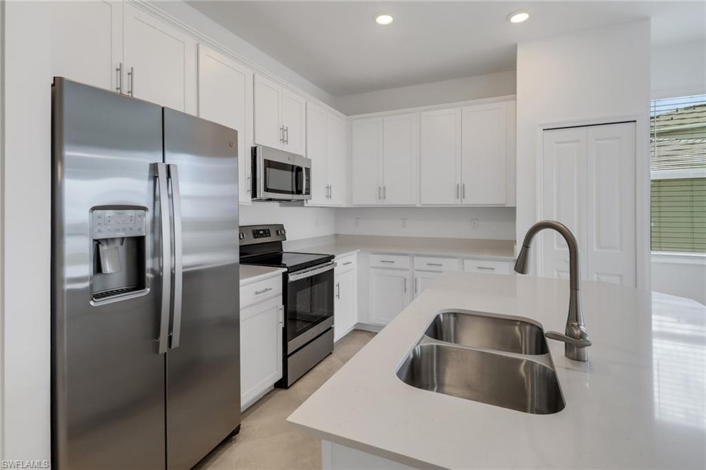 Modern kitchen featuring white cabinetry, stainless steel appliances, light countertops, a dual basin stainless steel sink, and recessed lighting