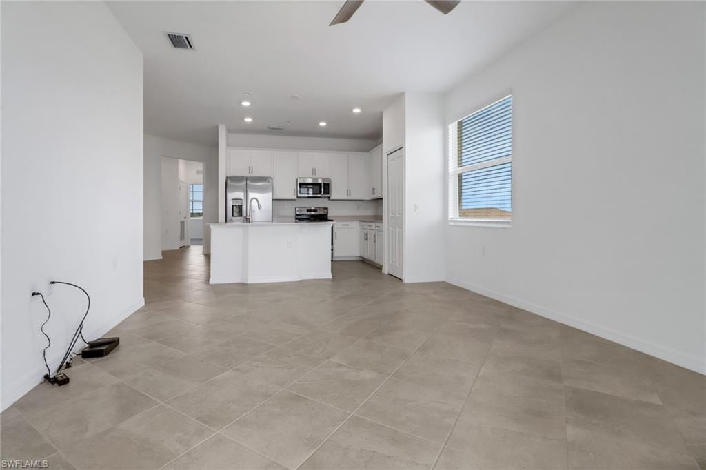 Open-concept living area featuring large format tile flooring, a kitchen island with sink, stainless steel appliances, white cabinetry, and recessed lighting