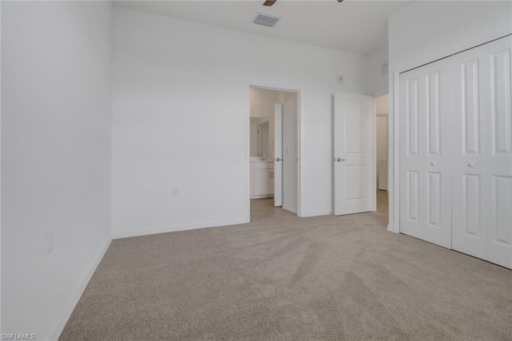 Carpeted room with white walls, featuring a white bi-fold closet and an open doorway leading to a bathroom with a white vanity and mirror