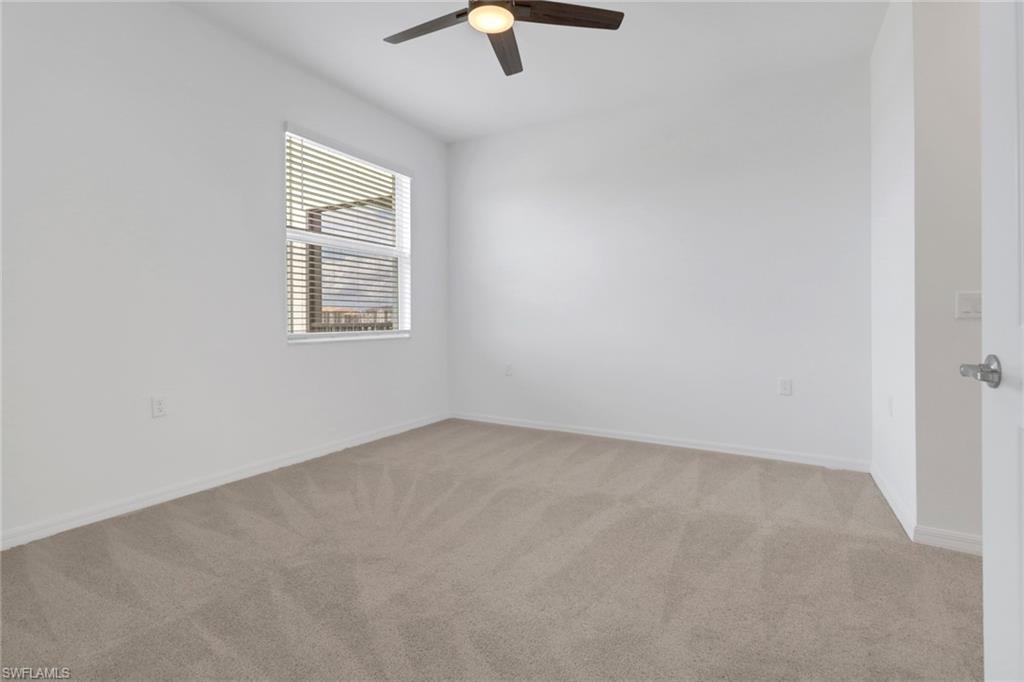 Spacious room featuring neutral carpeting, white walls, a single window with blinds, a ceiling fan with light fixture, and white trim