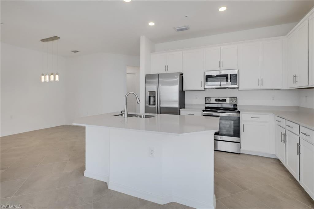 Modern kitchen featuring an island with a stainless steel sink and faucet, white cabinetry with silver hardware, light countertops, and stainless steel appliances including a refrigerator, range, and microwave