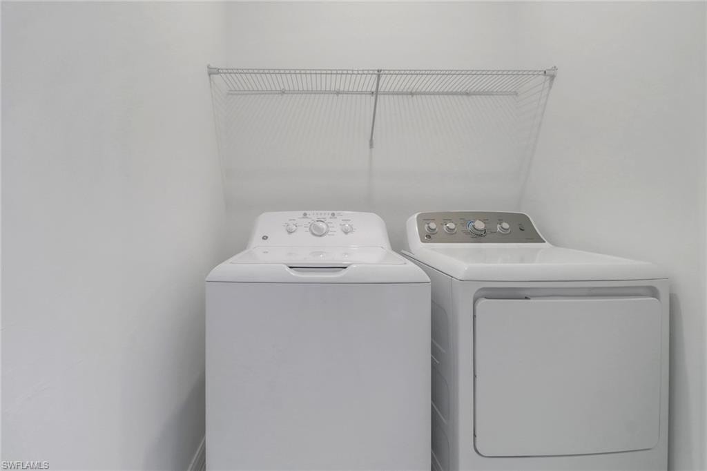 Dedicated laundry area featuring a washer and dryer set, white painted walls, and an overhead wire shelving unit