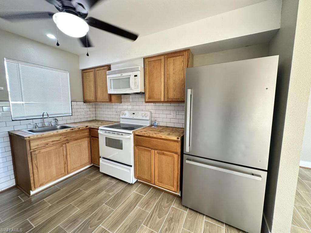 Kitchen with white appliances, wood finish cabinets, ceiling fan, wood finish floors, and decorative backsplash